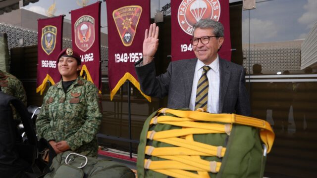 Ricardo Monreal saluda junto a una militar y equipo de paracaidismo durante una exhibición.
