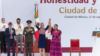Claudia Sheinbaum y Clara Brugada levantan las manos unidas en el templete del Zócalo, acompañadas de autoridades.