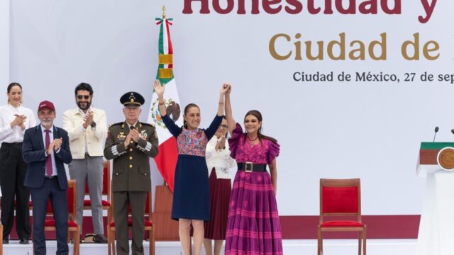 Claudia Sheinbaum y Clara Brugada levantan las manos unidas en el templete del Zócalo, acompañadas de autoridades.